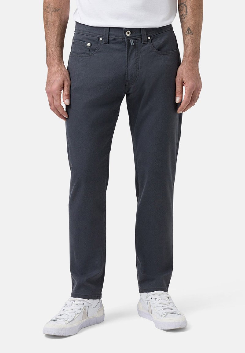 Pantalon en coton gris avec une coupe slim, design à cinq poches et coutures contrastées. Accompagné de baskets blanches.
