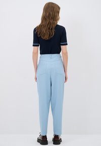 Marineblaue kurzärmlige Bluse mit hellblauen Akzenten, kombiniert mit hellblauen hoch taillierten Hosen. Die Hosen verfügen über Gesäßtaschen und gerade Beine.