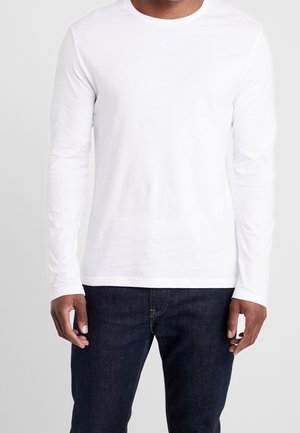 Weißes Langarm-T-Shirt mit Rundhalsausschnitt aus leichtem Stoff, kombiniert mit dunkelblauen Denim-Jeans. Schlichtes und minimalistisches Design.