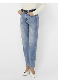 Jeans de tiro alto en azul claro con un corte clásico, que cuentan con bolsillos delanteros y un cinturón negro. Combinados con tacones cerrados blancos.