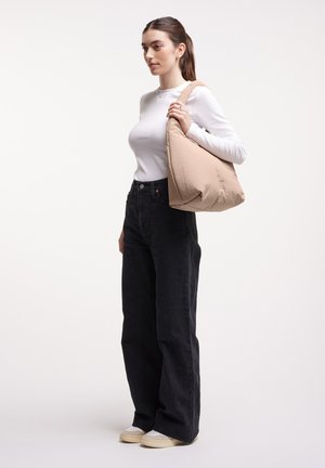 Bolso de hombro acolchado beige con una forma suave y redondeada. Presenta una sola correa y costuras mínimas. Llevado con jeans negros de cintura alta.