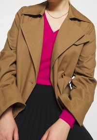 Brązowa podwójnie zapinana marynarka z dużymi klapami, zestawiona z różowym swetrem o fakturze i czarną plisowaną spódnicą, prezentująca miękkie materiały i kontrastujące kolory.