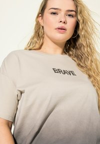 Béžové bavlněné tričko s tučným textem "BRAVE", krátkými rukávy a ombré designem, který na spodní části přechází do šedé. Hladká textura.