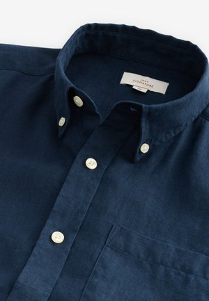 Tumesinine linane särk nööpidega alläärisel krael, valgete nuppude ja rinnataskuga. Omab tekstuuriga kangast detailsemaks väljanägemiseks.