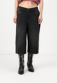 Culottes de ganga preta com cintura alta, bolsos frontais e um corte largo. Combinados com botas pretas com detalhes de estilo ocidental.