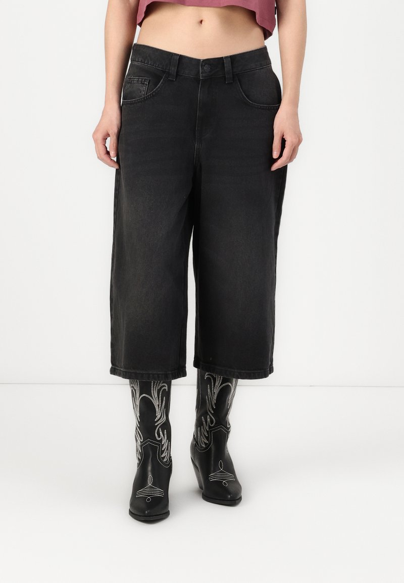 Culottes de ganga preta com cintura alta, bolsos frontais e um corte largo. Combinados com botas pretas com detalhes de estilo ocidental.
