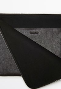 Sort læder clutch med lynlåslukning, der har en glat tekstur, og som har en kontrasterende sort stofforet samt et præget logo indeni.