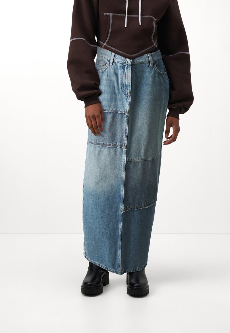 Jeans maxi szoknya foltos dizájnnal, világoskék és sötétkék árnyalatokkal, egyenes szabással és dísztűzéssel; fekete csizmával viselve.