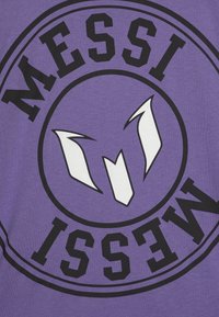 Violetinės spalvos medvilninė marškinėliai su apvaliu dizainu, kuriame paryškintais juodais žodžiais „MESSI“ ir centre baltu stilingu emblemą.
