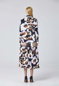 Cette robe à manches longues possède une jupe en tiers avec un imprimé floral abstrait audacieux en violet, blanc, marron et marine. Fabriquée en tissu lisse.