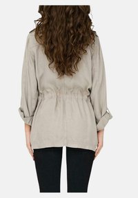 Chaqueta gris claro con un corte relajado, cintura ajustable con cordón y mangas enrolladas. Fabricada en una tela suave con una textura lisa, con un detalle mínimo.