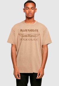 Tan katoenen t-shirt met "Iron Maiden Powerslave" graphic in bruin, met een ronde halslijn en korte mouwen.