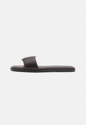 Brown leather slide sandals with a wide strap featuring a textured pattern. Flat sole with a smooth finish, minimalistic design.