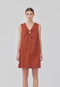 Robe sans manches couleur rouille avec décolleté en V profond, détail en trou de serrure à l'avant avec un nœud, et coupe droite, décontractée.