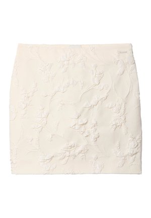 Minirok in crèmekleur met subtiele verhoogde bloemenborduursel en een klein metalen merkteken aan de rechterbovenkant.