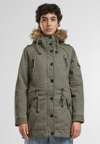 Olijf groene parka jas met faux bont capuchon, meerdere ritszakken, knoopsluiting, elastische trekkoorden en contrasterende stiksel.