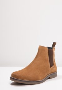 Béžové semišové Chelsea boty s elastickými bočními panely, zaoblenou špičkou a hnědou gumovou podrážkou. Disponují poutkem pro snadné obouvání.