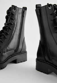 Svarta läderankelboots med snörning framtill och sidodragkedja, med en texturerad gummisula och en stabil klack.