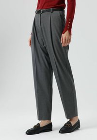 Grijze, hooggetailleerde plissébroek van een zachte stof. Voorzien van een zwarte riem, met een strak ontwerp en taps toelopende pijpen.