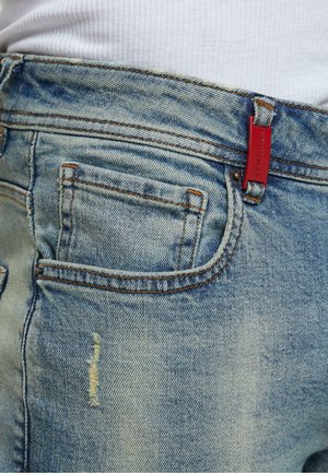 Jeans in denim azzurro chiaro con un'etichetta rossa, primi piani della tasca posteriore e visibili segni di usura sul tessuto.