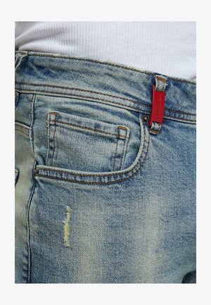Jeans in denim azzurro chiaro con un'etichetta rossa, primi piani della tasca posteriore e visibili segni di usura sul tessuto.