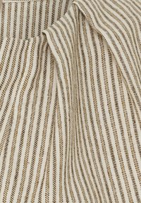 Bomuldsstof med tynde, skiftende striber i beige og creme; let tekstureret overflade; viser bløde folder og draperinger.