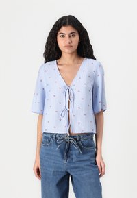 Blåstripet kortermet bluse med små røde blomsterbroderier og en frontknute. Båret med høyhalsede jeans.