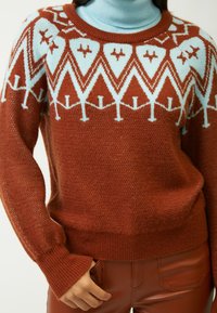  Rostfarbener Pullover mit hellblauen geometrischen Mustern, dicke Stricktextur, gerippte Bündchen und Saum, über einem blauen Rollkragenpullover getragen.