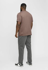 Brun bomulds T-shirt med rund hals, parret med grå løstsiddende bukser og sort-hvide sneakers, set fra ryggen.