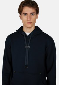 Felpa con cappuccio di un blu scuro, realizzata in tessuto morbido, dotata di tasca a marsupio, cordini regolabili e un'etichetta del marchio sul collo.