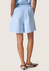 Ljust blå randiga shorts med elastisk midja, tillverkade av strukturerad tyg, matchade med svarta sandaletter med remmar. Bakifrån visas en längd till mitten av låret.