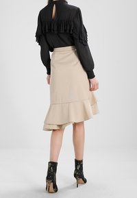 Svart blus med volangärmar, beige lager-skirt och svarta blommönstrade ankelstövlar, med höga klackar och en nyckelhålsdetalj på baksidan.