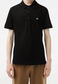 Polo noir avec col classique, manches courtes, patte de boutonnage à trois boutons et logo brodé subtil sur la poitrine. Matière en coton doux.