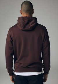 Sudadera de algodón burdeos con un bolsillo canguro en la parte delantera y capucha ajustable con cordón. Presenta puños y dobladillo acanalados, textura suave.