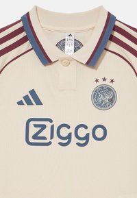Béžové polo tričko s maroonovými a modrými akcenty, se zapínacím límcem, logem Adidas, brandingem Ziggo a klubovým emblémem se třemi hvězdami.