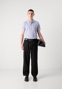 Hellblaues Poloshirt mit weißen Akzenten, schwarze weite Hose und schwarze Schuhe. Hält eine schwarze Tasche. Einfaches Design, lässiger Look.