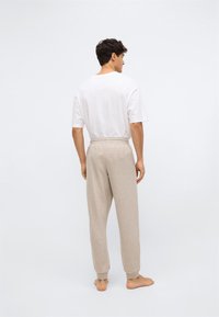Herenoutfit met een losse pasvorm, bestaande uit een eenvoudig wit katoenen T-shirt en beidge gebreide joggingsbroek met elastische tailleband en manchetten, gezien vanaf de achterkant.