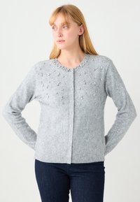 Grijze cardigan gemaakt van zachte stof, met een ronde hals en decoratieve kralen langs de voorkant. Lange mouwen en knoopsluiting.