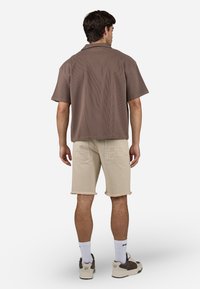 Brun kortærmet skjorte med ribbet tekstur, parret med beige denimshorts med frynset kant og dekoreret stikning på lommerne.