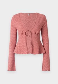 Röd texturerad långärmad topp med djup V-ringning, samlad knytning vid midjan och en peplumkjol med scallopkant.