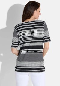 Haut à manches courtes noir et blanc avec des rayures et des pois de différentes épaisseurs et placements, fabriqué à partir d'un tissu léger et doux.