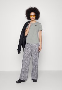 Pilkos Nike marškinėliai, juodas bomber tipo švarkas numestas ant peties, ir plačiakurpės pilkos kelnės su zebra raštu. Geltonos saulės akiniai ir juodi batai.
