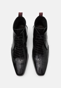 Botas de tobillo de cuero negro con un acabado brillante, que presentan paneles texturizados de cocodrilo, diseño de ala y detalles perforados. Tirador rojo.
