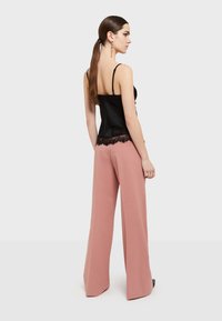 Zwarte satijnen camisole met kantafwerking, gecombineerd met hoge, wijde, roze broek. Gladde textuur, eenvoudig ontwerp.