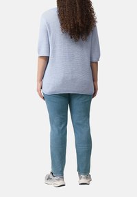 Lichtblauwe gebreide trui met korte mouwen en een losse pasvorm, gecombineerd met lichtblauwe jeans en grijze sport schoenen.