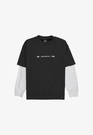 Černý krátký rukávový svetr vrstvou přes světle šedou košili s dlouhým rukávem a bílým textem a logy Quiksilver umístěnými uprostřed hrudi.