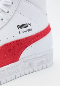 Vita hög sneaker med röd mockadetalj, med en texturerad vit sula, svart Puma-logotyp och "R. Sampson"-branding.