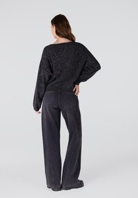 Zwarte gebreide trui met een losse pasvorm en lange mouwen, gecombineerd met hoge, wijde zwarte jeans en robuuste zwarte laarzen.