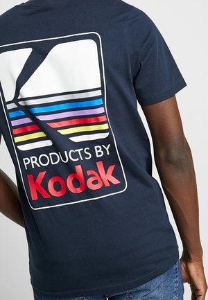 Navy blue t-shirt with a large white, red, and colorful striped logo on the back reading “Products by Kodak.” Short sleeves, cotton material.