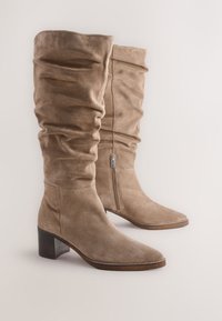 Bottes montantes en daim tanné couleur fauve avec un design décontracté, bout carré et talon bloc. Dotées d'une fermeture éclair latérale pour faciliter l'enfilage.